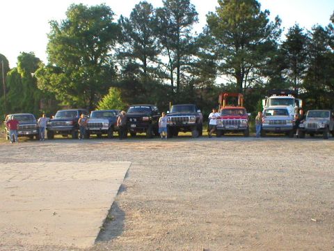 1989 Ford Bronco - A collection of trucks and SUVs are lined up outdoors with people standing near them.
