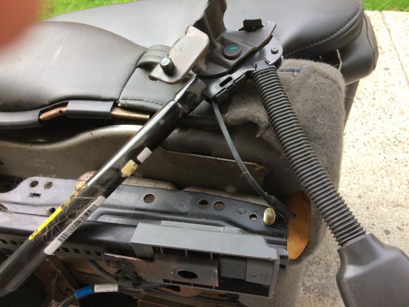 Underside of a car seat showing metal frame, seat belt mechanism, and wiring.