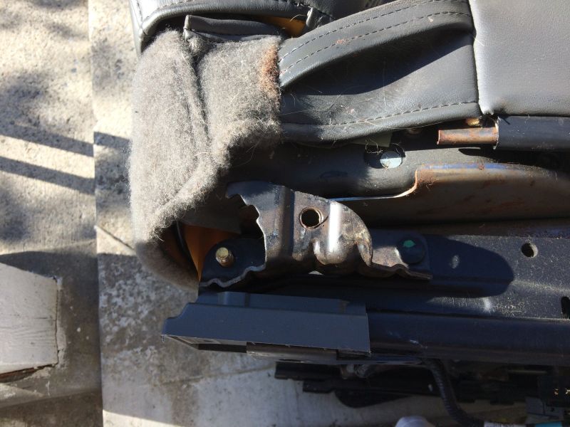 Close-up of a rusted car seat bracket with worn fabric.