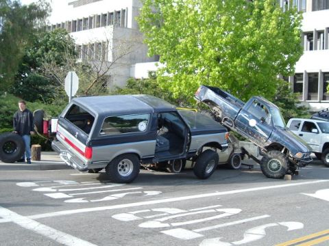 1989 Ford Bronco - A 1989 Ford Bronco is being towed by a lifted pickup truck, with a person standing nearby holding a spare tire.