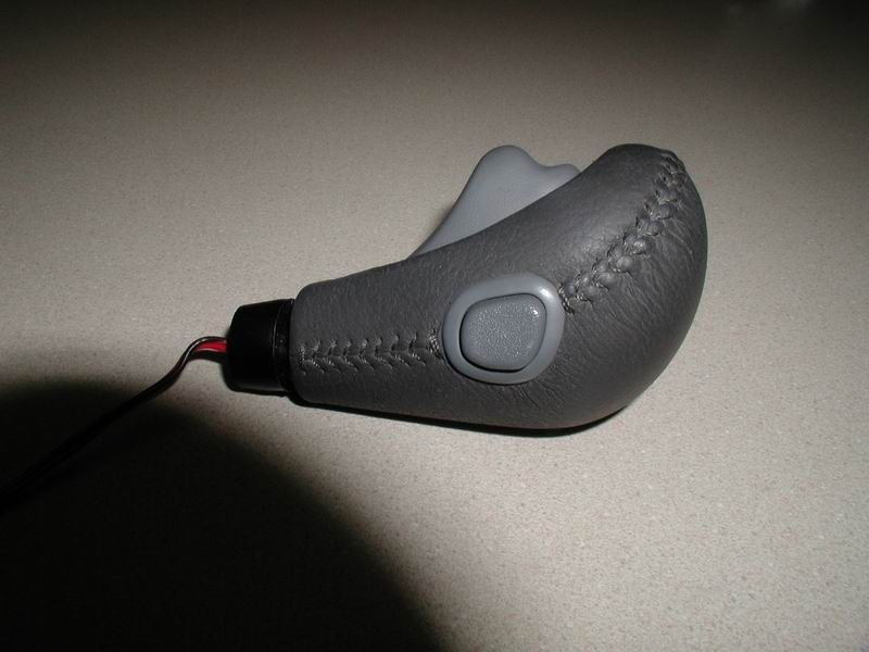 Gray leather shift knob with stitching and button, wires visible.