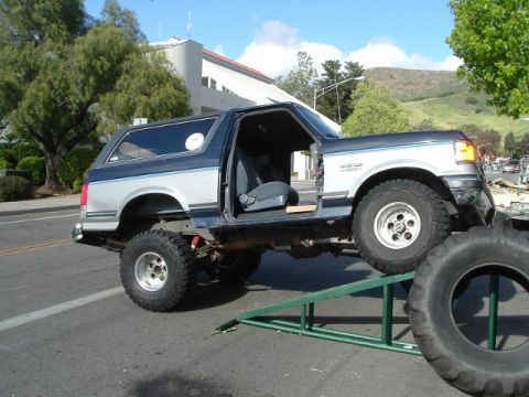 1989 Ford Bronco - A lifted Ford Bronco is positioned on green ramps, with its driver's side door open.