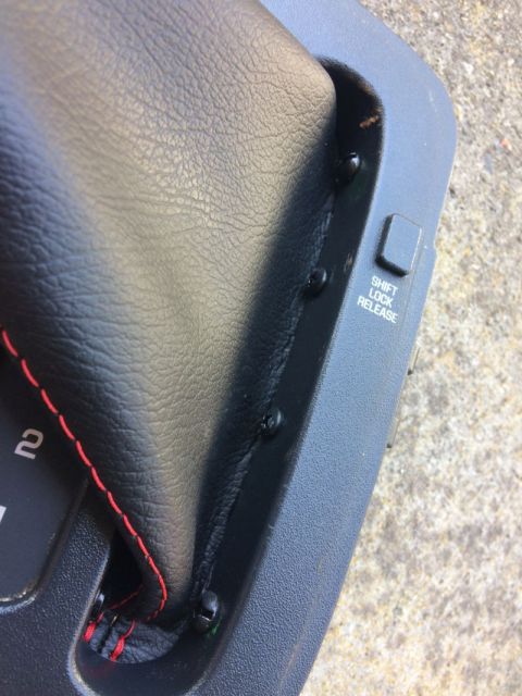 2002 Pontiac Grand Prix - A close-up view of a black leather shift boot with red stitching, attached to a black plastic console. A small button labeled "SHIFT LOCK R…