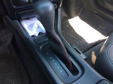 2002 Pontiac Grand Prix - The interior of a car's center console is shown, focusing on the automatic gear shifter with red stitching. A white cloth is visible in the…
