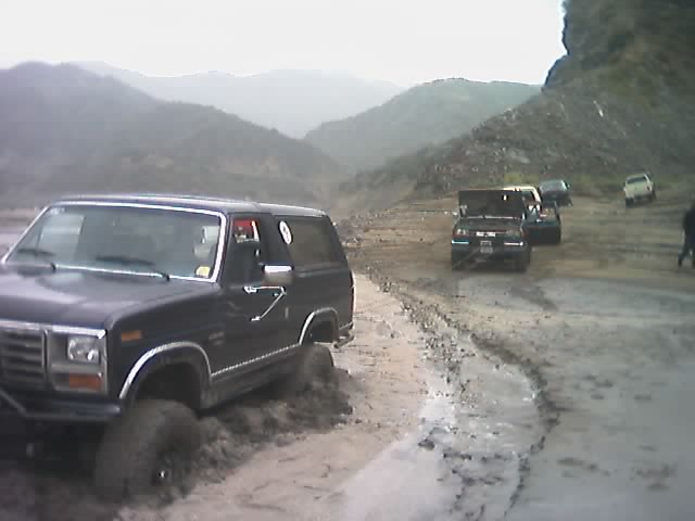 Dark lifted two-door Ford Bronco on muddy trail with other trucks in a canyon