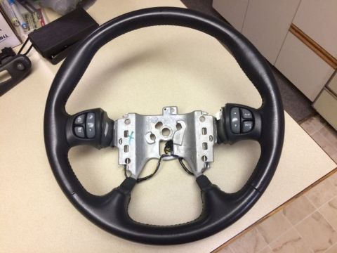2002 Pontiac Grand Prix - A black leather steering wheel with integrated audio controls is shown on a table. The steering wheel has a metal mounting bracket attached…