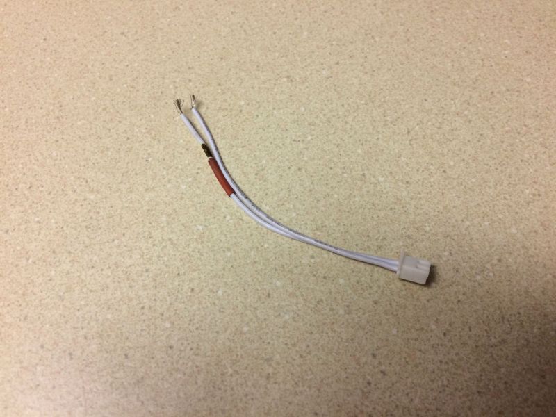 White wire harness with connector and exposed wires on a speckled surface.
