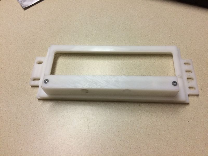 White plastic rectangular frame with screw holes on a speckled countertop.