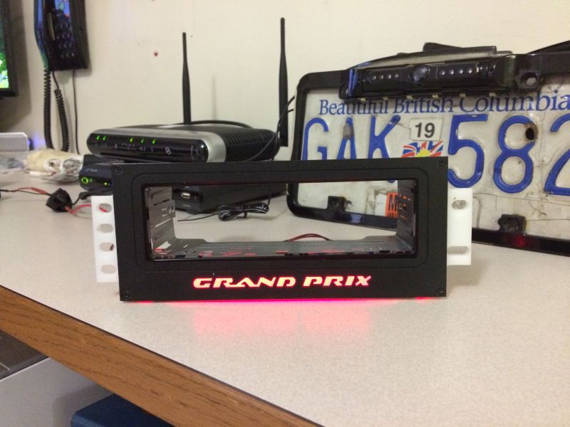 Custom car stereo bracket with red illuminated "GRAND PRIX" text, BC license plate, and backup camera.