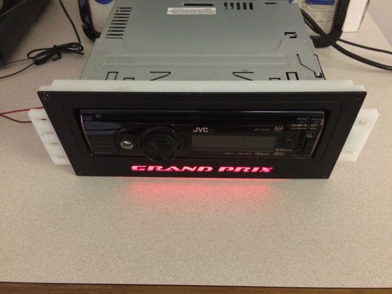 JVC car stereo with custom black bezel and red "GRAND PRIX" lettering in a white dash kit.