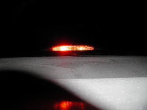 2002 Pontiac Grand Prix - A close-up shot of a red, illuminated third brake light mounted on the rear of a vehicle. The light is reflecting on the dark, glossy surfa…
