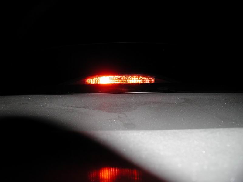 Red third brake light illuminated on a dark vehicle surface with reflection.