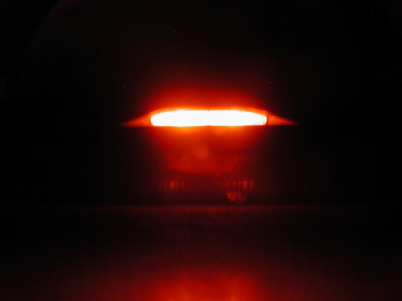 Illuminated red taillight on a dark background.