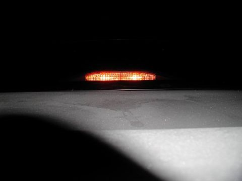 2002 Pontiac Grand Prix - A close-up, low-angle shot shows the illuminated amber brake light on the rear of a dark-colored vehicle at night. The light is a horizonta…