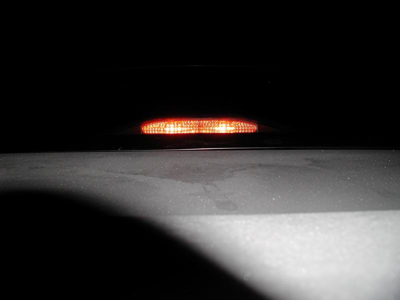 Illuminated amber brake light on a dark vehicle at night.