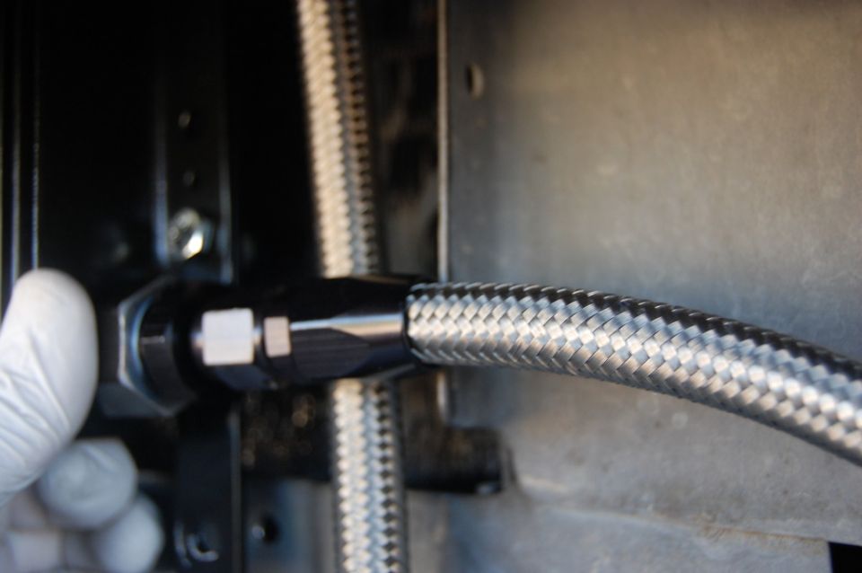 Close-up of a braided metal hose and black fitting being connected to a vehicle component.