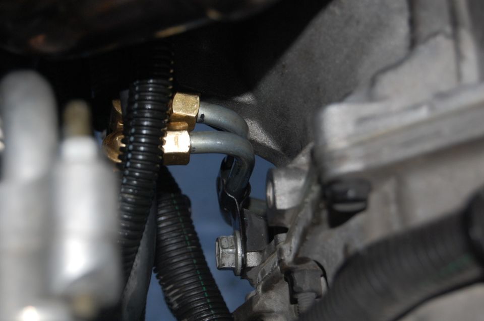 Brass fittings on metal fuel lines attached to engine component with bracket and bolt.