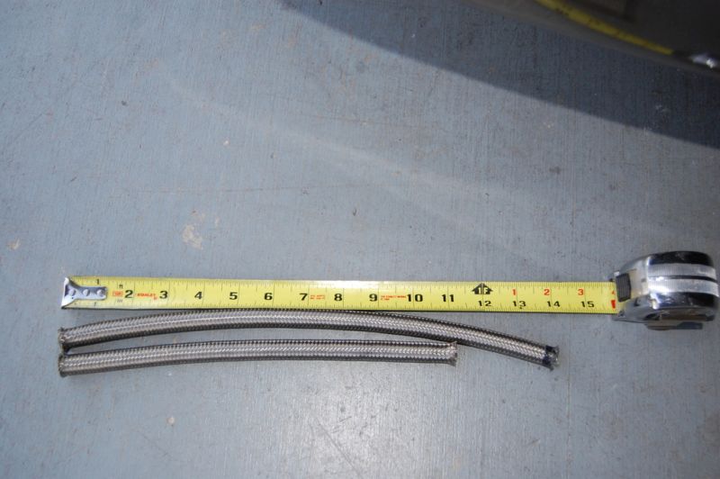 Two braided hoses next to a measuring tape on a concrete floor.