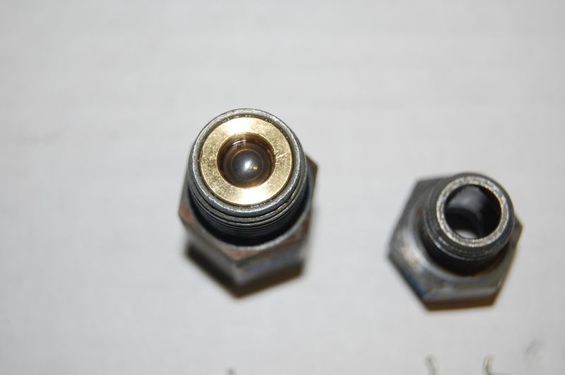 Two metal fittings, one with a brass ring and ball bearing, against a white background.