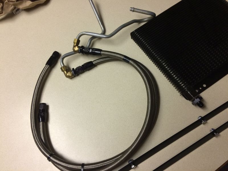 Black oil cooler with braided lines and fittings, next to mounting brackets.