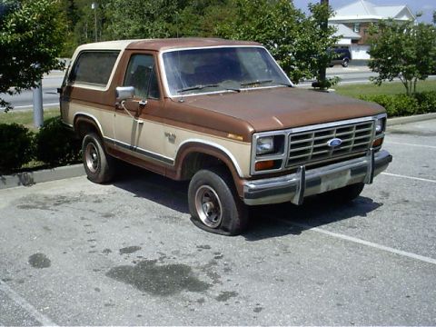 1985 Ford Bronco - This 1985 Ford Bronco has a flat tire and is parked in a lot.
