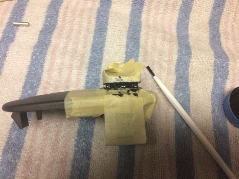 Car part being painted black with a brush and masking tape.