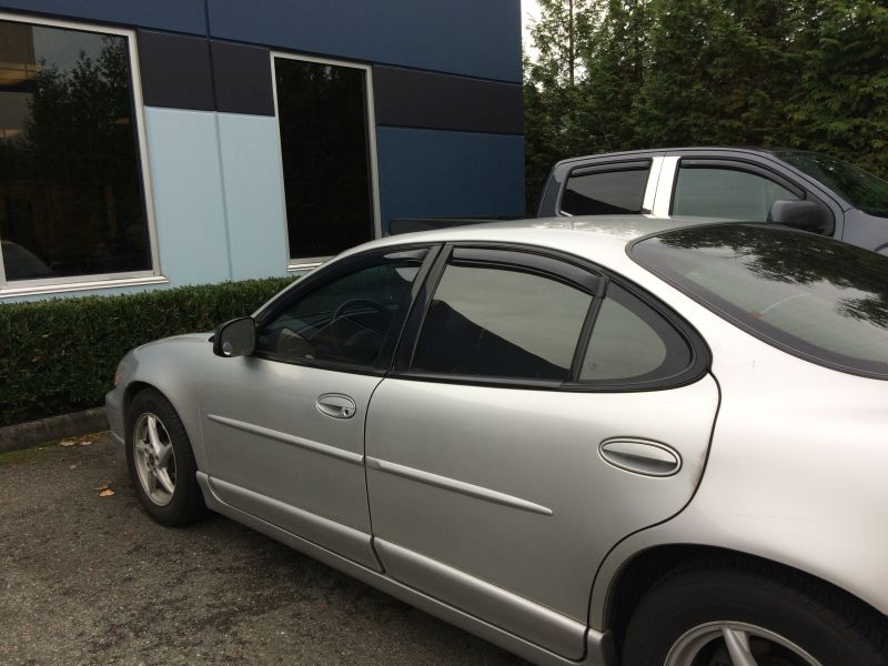 Silver 2002 Pontiac Grand Prix parked outside a building with a pickup truck behind it.