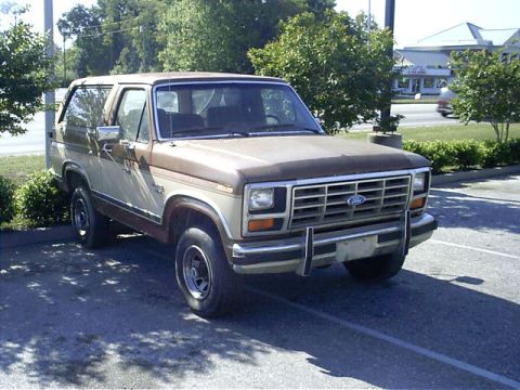 1985 Ford Bronco - This two-tone brown and tan Ford Bronco is parked in a lot, showing its front three-quarter view.