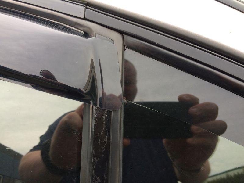 Close-up of car window trim with reflection of person holding phone