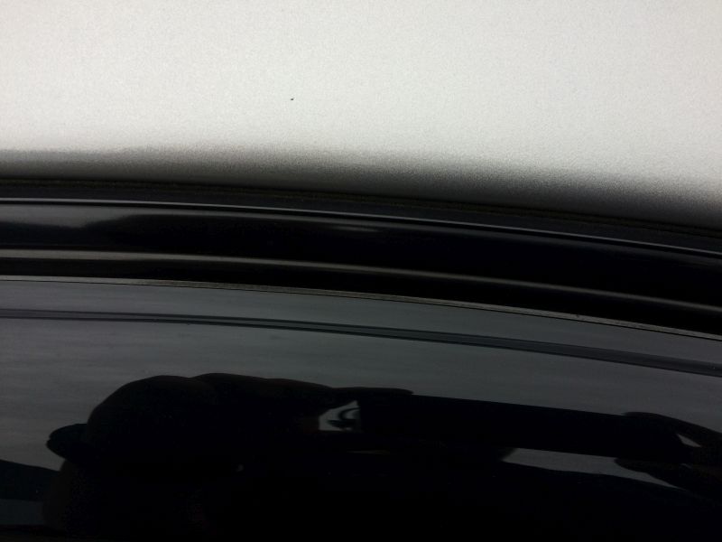 Reflection of a hand in the black car roof and window frame.