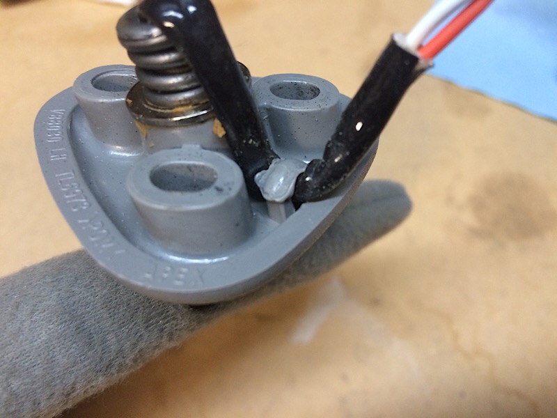 Gray plastic automotive part with wires and spring, showing molded text.