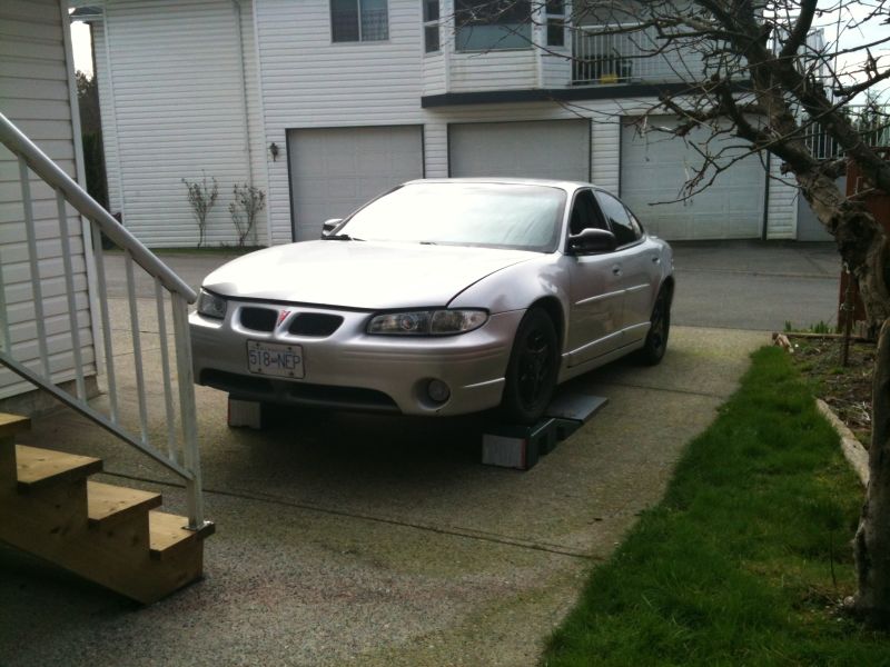 Silver 2002 Pontiac Grand Prix on car ramps in a driveway.