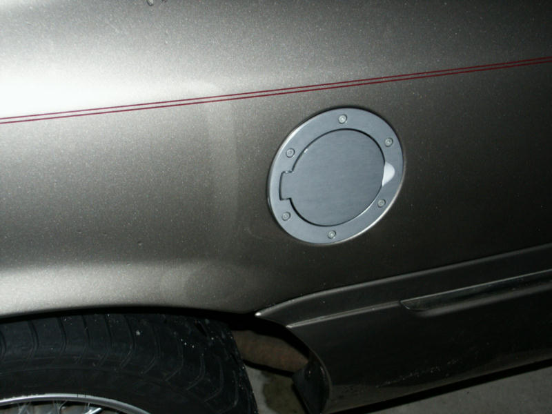 Round billet aluminum fuel door on tan sedan quarter panel with red pinstripe