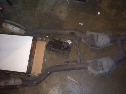 1991 Ford LTD Crown Victoria - Two catalytic converters and exhaust pipes are laid out on a concrete floor next to a white box.