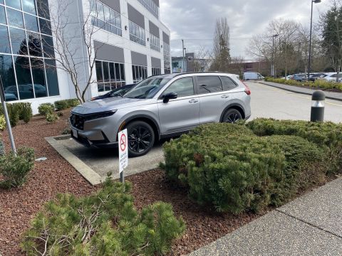 2026 Honda CR-V - A silver Honda CR-V is parked in front of a modern office building. A "No Smoking" sign is visible in front of the vehicle.
