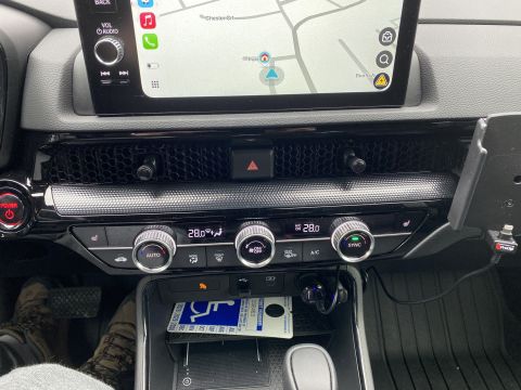 2026 Honda CR-V - The interior of a modern car's center console is shown, featuring a touchscreen display, climate control knobs, and a charging port.