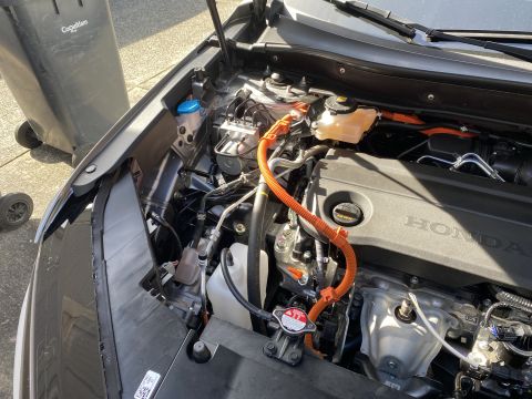 2026 Honda CR-V - The engine bay of a Honda CR-V is shown, with the hood open. Visible components include the engine cover with Honda branding, orange high-v…