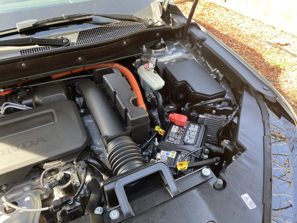Engine bay of a Honda CR-V showing battery, air intake, and orange high-voltage wiring conduit.