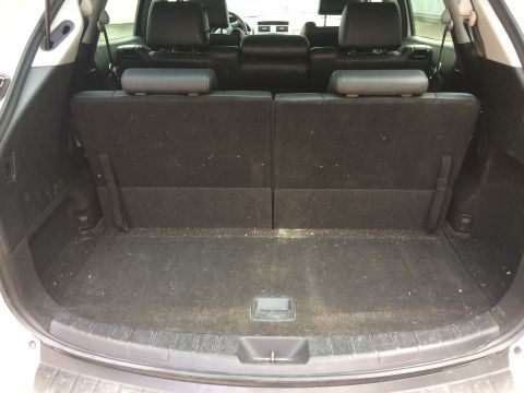 Interior rear cargo area of a white SUV with seats folded down, showing dark fabric floor with debris.