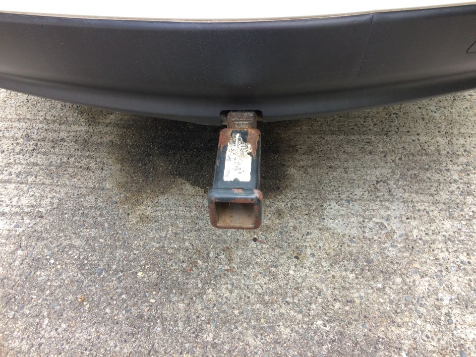 Rusty trailer hitch receiver under a black bumper on a vehicle.