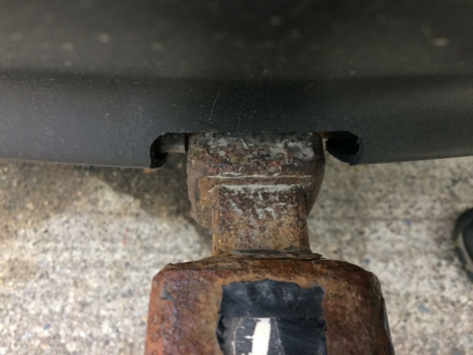 Close-up of a rusty trailer hitch receiver attached to a black plastic bumper.
