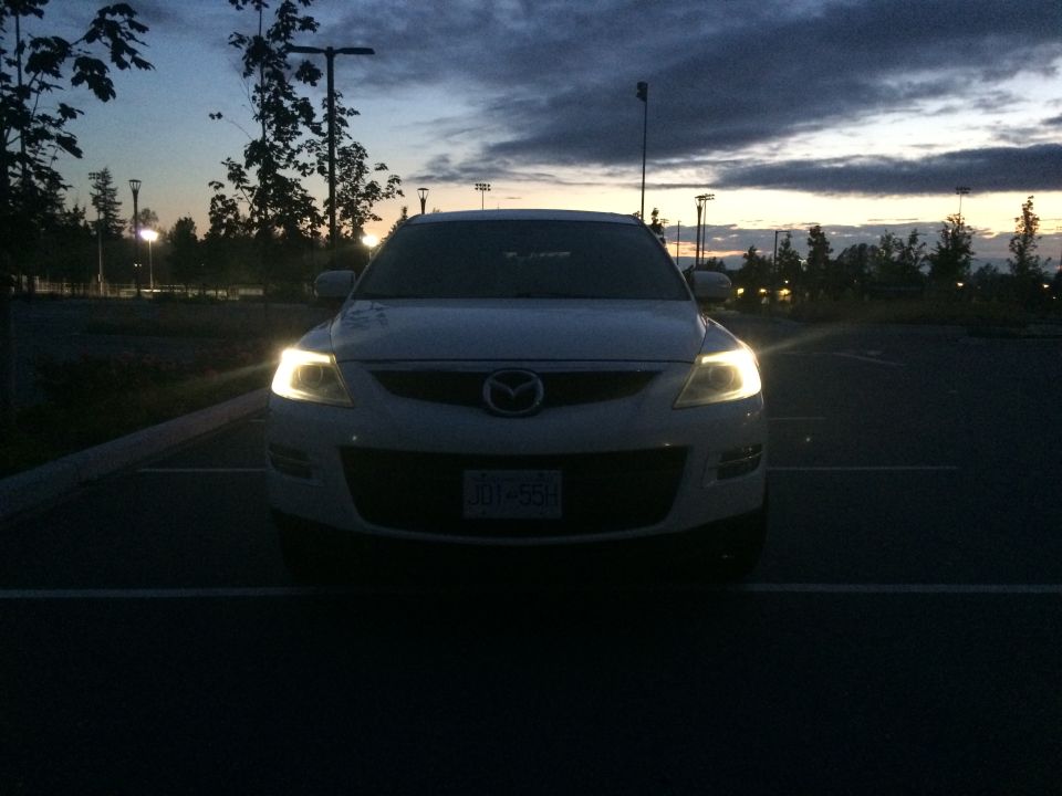 White 2009 Mazda CX-9 parked in a lot at dusk with headlights on.