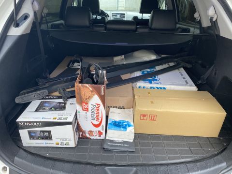 2009 Mazda CX-9 - The open trunk of a white SUV is filled with various items, including car audio equipment boxes, a box of protein powder, and what appear t…