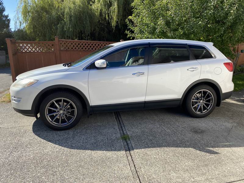 White Mazda CX-9 SUV parked on a concrete driveway, side view.