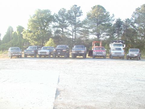 1988 Ford Bronco - Several trucks and SUVs are lined up in a parking lot on a sunny day.