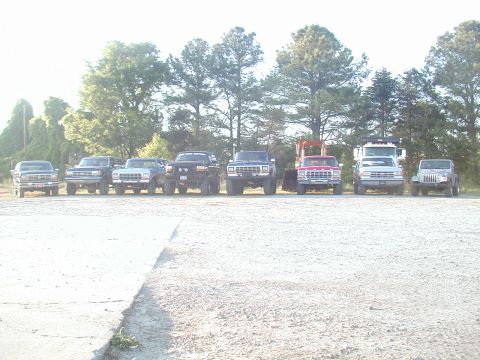 1988 Ford Bronco - Multiple trucks and SUVs are lined up outdoors on a sunny day.