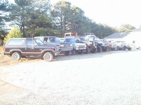 1988 Ford Bronco - Several trucks and SUVs are parked in a lot on a sunny day.