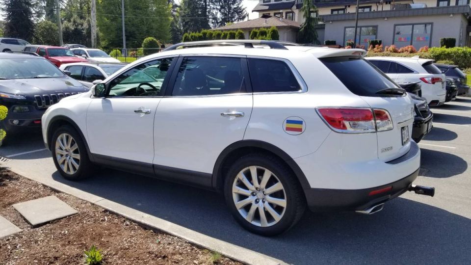 White 2009 Mazda CX-9 SUV with Ukrainian flag sticker and trailer hitch receiver.