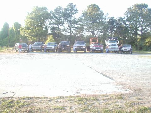 1988 Ford Bronco - A collection of trucks and SUVs are parked in an outdoor lot under a bright sky.