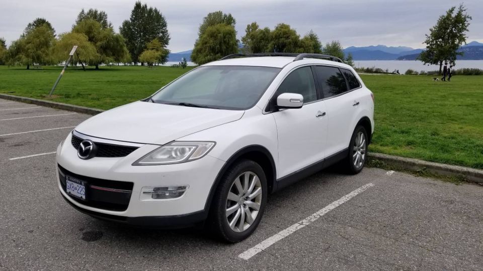 White 2009 Mazda CX-9 parked in a lot with a park and water view.
